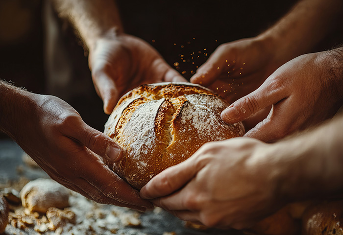 A boule of floured bread being shared with outreached hands