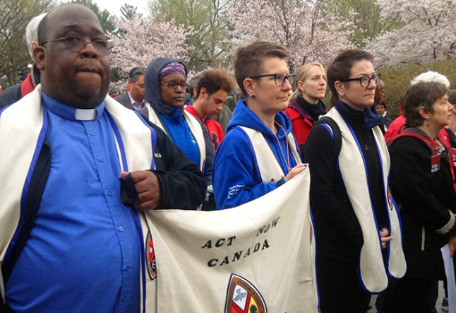 United Church leaders marching and holing a sign stating "Act against racism"
