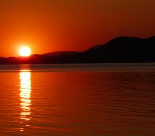 A picture of a sunset over water with mountains in the background. A deep red-orange colour saturates the evening scene.