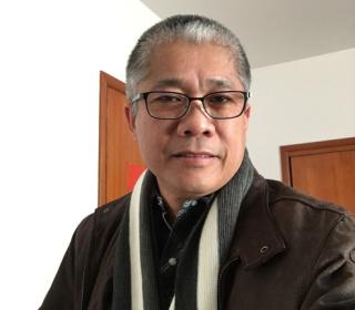 The author, Noel A. Suministrado, a Filipino man with short dark hair with streaks of grey. Wearing glasses and a scarf.