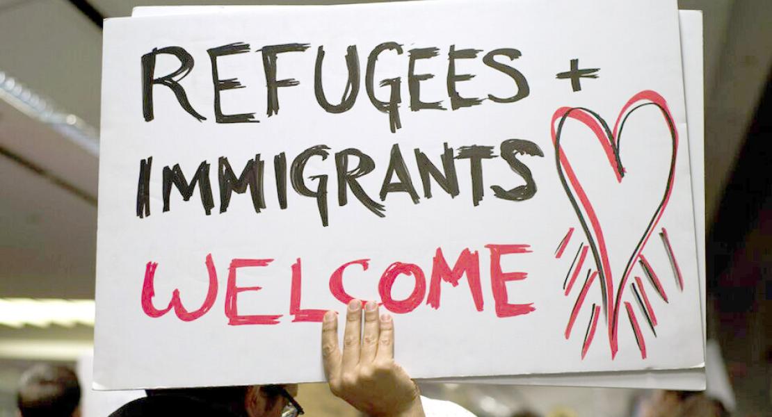 Person holding a sign that says "Refugees and Immigrants Welcome"