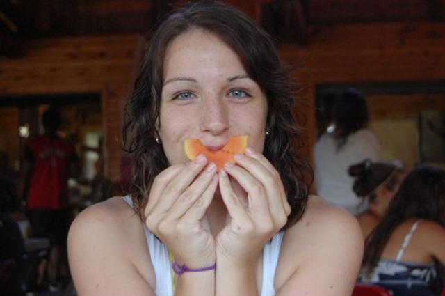 A teenager holds a slice of orange in the shape of a smile in front of her mouth.
