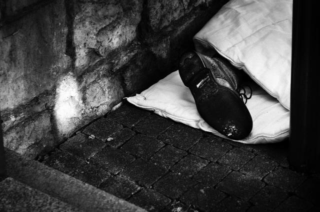 A man's foot peeks out of his blanket, as he sleeps on the street.