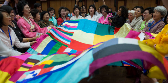Women mobilize for peace in Korea, gathered around a large multi-coloured fabic during a demonstration.