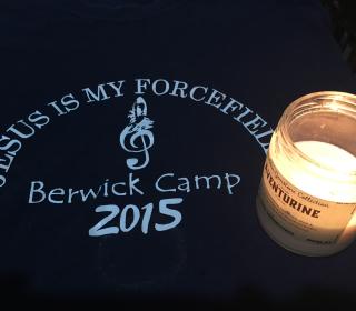 A candle sits upon a black cloth memento, which says "Jesus is my Forcefield, Berwick Camp, 2015.