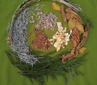 A beautiful photo of sacred medicines from both the Near East and Indigenous traditions laid out in a circle on a green cloth background..
