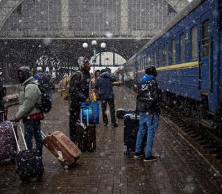 Several Nigerian students with their luggage stand in front of a train at the Lviv station in a snowfall.