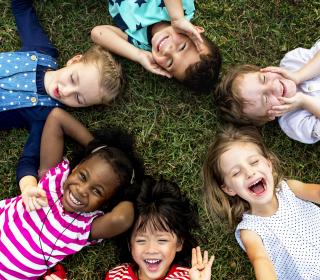 A diverse group of kids smile together while laying in a circle at a playground.