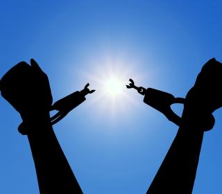 A pair of arms rise in triumph against a blue sky, breaking the chains of enslavement.