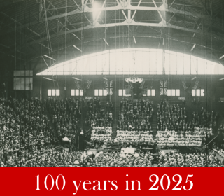 People fill an arena in a black and white photo from 1925. The words "100 years in 2025" are on a red background below.