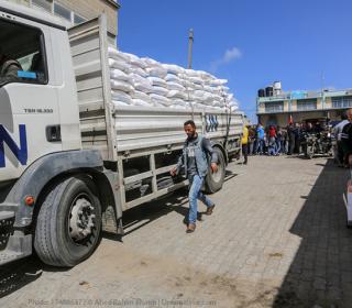 A large UN aid truck is loaded with bags in front of a refugee camp.