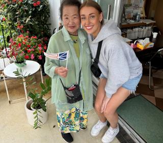 An elderly woman holding a Newfoundland flag poses with a young woman.