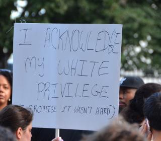 A white woman holds a sign that says, "I acknowledge my white privilege" during a protest.