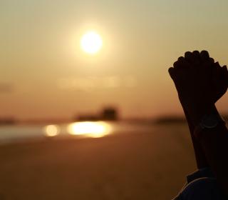 A pair of hands of a person praying in the sun by the sea.