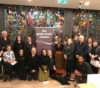 This photo shows a group of 19 diverse people of differing backgrounds and types of abilities in front of a large multi-coloured stained glass. Included in the group are those who participated in the conversation on inclusion. conversation