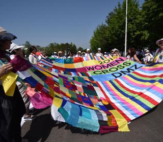 WomenCrossDMZ unfurl a colourful quilt during a march calling for peace in Korea/