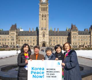 A group of five women pose in front of the tower at Parliament Hill in Ottawa on a brilliant cloudless day, where they advocated for peace in the Korean peninsula.