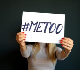 A white woman with blond hair holds a sign saying "#MeToo" in front of her face. 