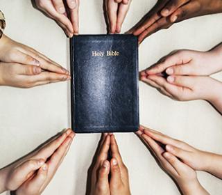 Praying hands around a bible