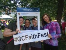 Three young people at the Festival of Faith hold a cardboard frame around themselves which has the #GCFaithFest tag in Oshawa during GC43.