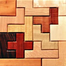 A puzzle of wooden pieces, each a different colour and angular shape, including one dark brown piece in the shape of a cross.