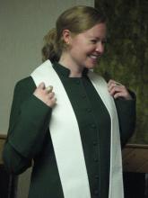 The author, a woman in a green dress with a white stole and with blond hair pulled back, smiles broadly at her ordination.