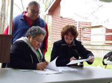 General Secretary Nora Sanders and Chief Denise Stonefish sign the document at a table outside.