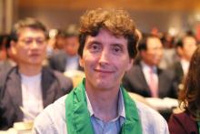 A portrait of John Egger, a young white man with curly hair and a green scarf. He is serving in global mission service in Korea.