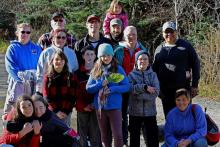 A group from Knox United on a on a hike on Tunnel Island pose together for a photo. A young girl in the middle of the group holds a green leaf.