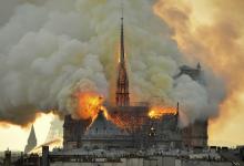 Huge flames consume the spire and roof of Notre Dame cathedral, while smoke towers over the city of Paris.
