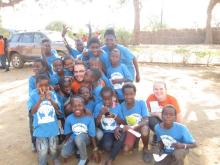 A group of children surround two Canadian visitors to Zambia for a photo.
