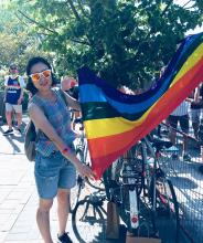The author outside with a bicycle by her side, holds a rainbow flag.
