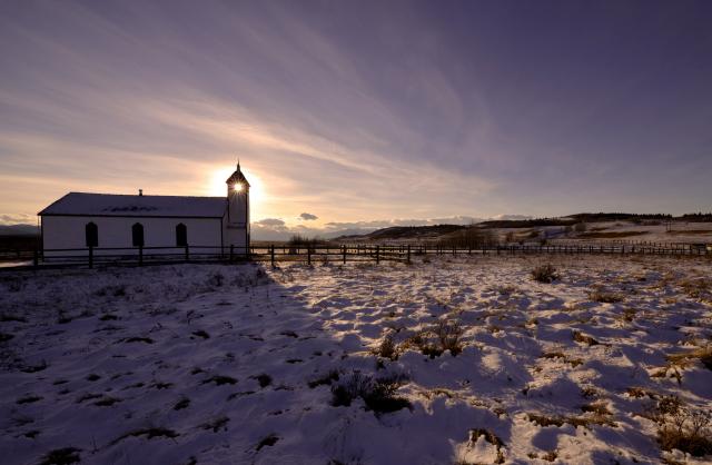 The sun shines through the bell tower of McDougall United Church in the snow covered landscape of Morely, Alberta.