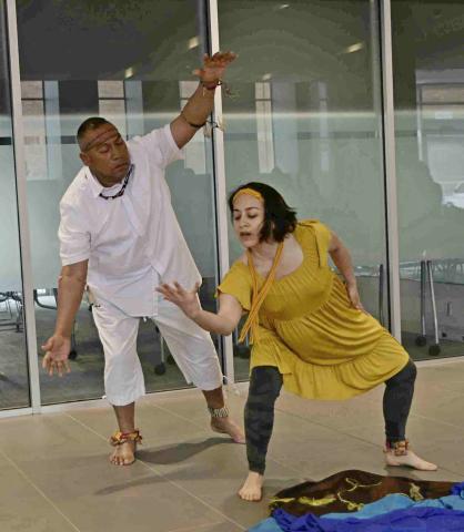 Two Latinx dancers in traditional farmworker dress, performance The Sunflower Dance. The woman depicts a growing sunflower, while the man standing over her depicts the sun.