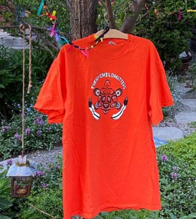 An orange t-shirt with the words Every Child Matters hangs in a tree in a garden