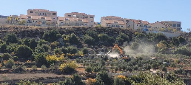 Homes being demolished by yellow heavy equipment, seen in a wide-angle photo from a distance across a desert valley. Expensive, modern homes line the ridge overlooking the scene.lley.