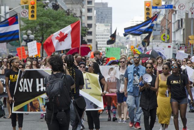 Black Lives Matter supporters march at Toronto Pride 2016. Black Lives Matter supporters march at Toronto Pride 2016, beneath a large Canadian flag and flags representing the Trans movement.