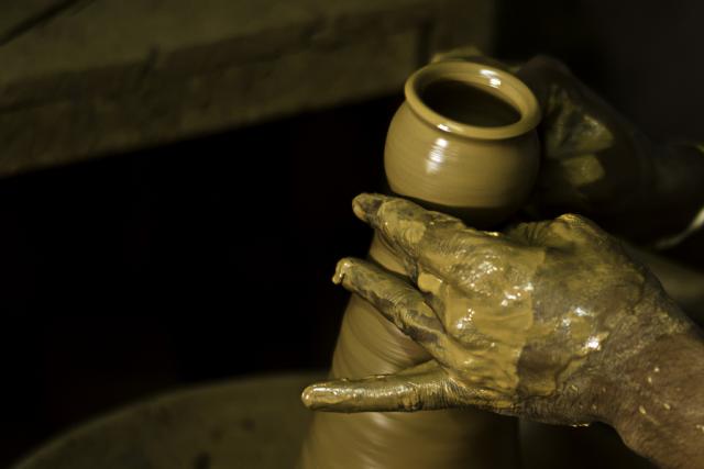 A potter's hands covered with wet clay and shaping a vessel on the pottery wheel in India.
