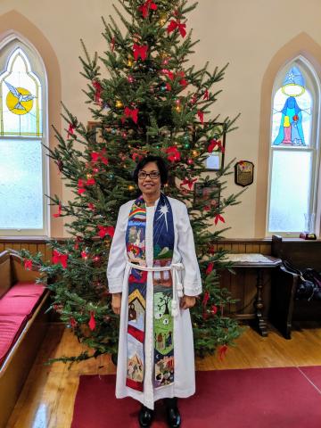 Rev. Dr. Margaret MacDonald, ordained minister standing in front of a Christmas tree
