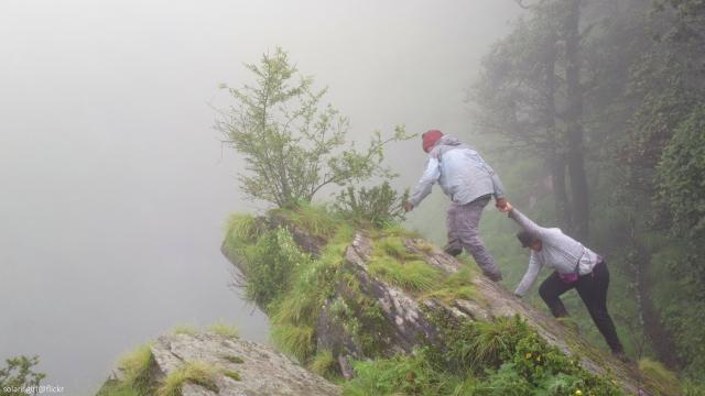 Only by working together can we be effective in achieving real and lasting change. Two people work collaboratively to climb over a rock on a foggy forest mountain.