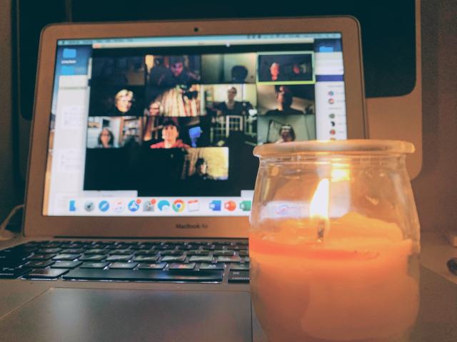 An online meeting of St. Matthew’s United Church, Toronto A lit candle is in front of a laptop that displays a Zoom meeting in progress.