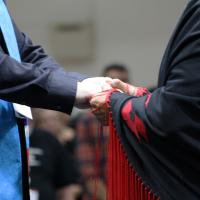 The hands of someone wearing a minister's stole and another person wearing an Indigenous shawl are clasped. 