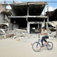 A boy rides a bike past ruined buildings in Khan Yunis
